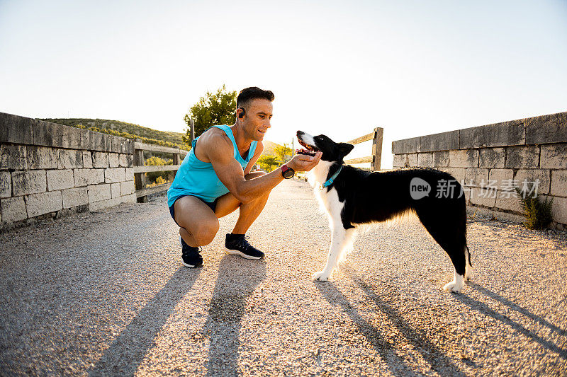 An adult man with an amputated arm in sportswear bends down to pet his dog outdoors. The dog is a black and white border collie breed. Dog walking concept.